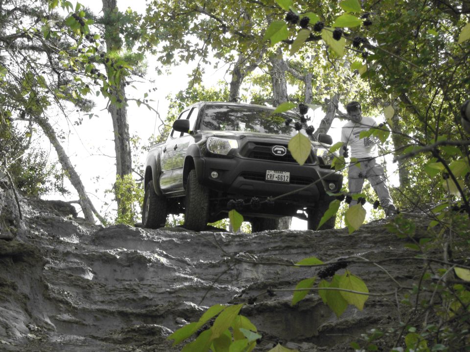 Black pickup truck navigating a steep, muddy trail with a person standing nearby
