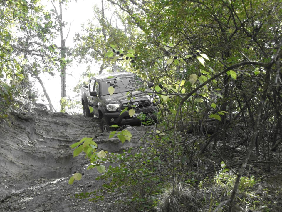 Dark pickup truck on a muddy, wooded trail. Front grille and headlights are visible
