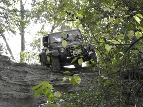 1995 Ford Bronco - A black Jeep Wrangler tackles a challenging off-road trail, its tires gripping the loose dirt as it climbs.