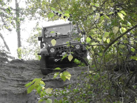 1995 Ford Bronco - A Jeep Wrangler navigates a steep, wooded trail.