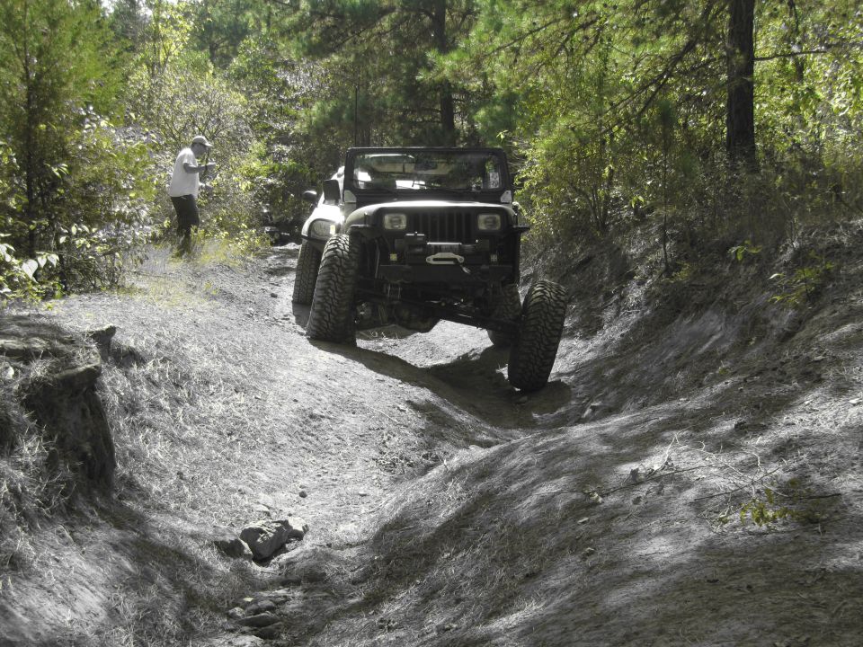 Black Jeep Wrangler with large tires driving on a dirt path, front view