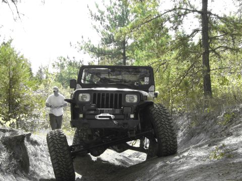 1995 Ford Bronco - A black Jeep Wrangler navigates a challenging dirt trail with a person standing close by.
