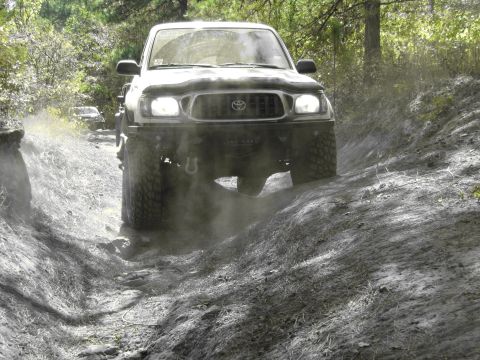 1995 Ford Bronco - A white Toyota Tacoma navigates a dusty off-road trail, with another vehicle following behind.