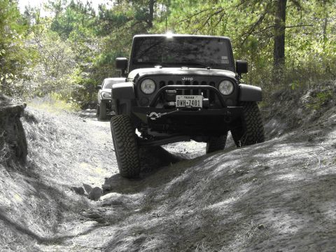 1995 Ford Bronco - A black Jeep Wrangler navigates a rough dirt trail with another vehicle following closely behind.