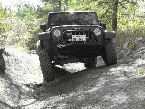 1995 Ford Bronco - Black Jeep Wrangler navigating a rough dirt trail with one wheel lifted.