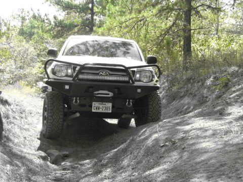 1995 Ford Bronco - This Toyota Tacoma is equipped with an aggressive aftermarket bumper and light bar, navigating a challenging off-road path.