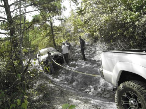 1995 Ford Bronco - Two trucks navigate a challenging dirt path, with one vehicle assisting the other.