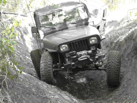 1995 Ford Bronco - A black Jeep Wrangler navigates a steep dirt trench during an off-road excursion.