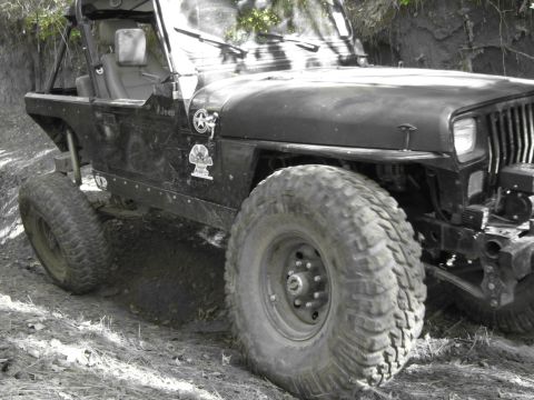 1995 Ford Bronco - A modified Jeep Wrangler with off-road tires navigates a muddy path.