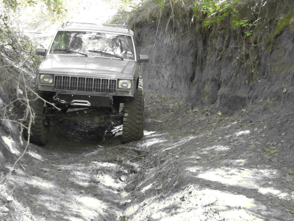 Gray Jeep Cherokee XJ with large tires driving on a dirt path