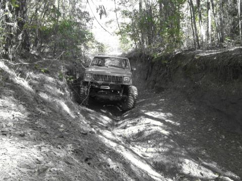 1995 Ford Bronco - A modified Jeep Cherokee XJ navigates a steep, wooded off-road trail.