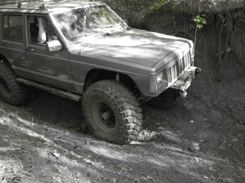 1995 Ford Bronco - A Jeep Cherokee XJ navigates a steep, muddy incline during an off-road excursion.