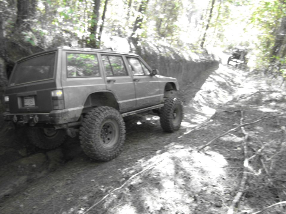 Modified Jeep Cherokee XJ on a wooded trail, with another vehicle in the distance