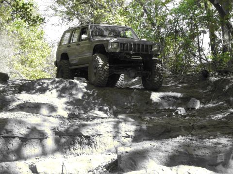1995 Ford Bronco - A modified Jeep Cherokee XJ navigates a challenging off-road trail with large tires and a lifted suspension.