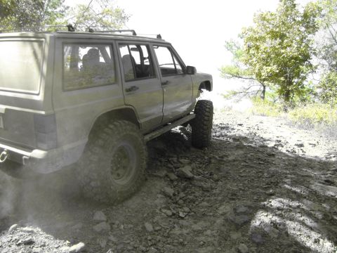 1995 Ford Bronco - This modified Jeep Cherokee XJ is navigating a rough, off-road path with large tires.