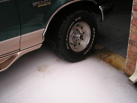 1996 Ford Bronco - Close-up of a 1996 Ford Bronco's front wheel and side panel, parked indoors.