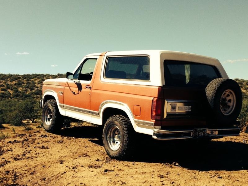 Orange and white Ford Bronco parked on a dirt hill, spare tire on the back