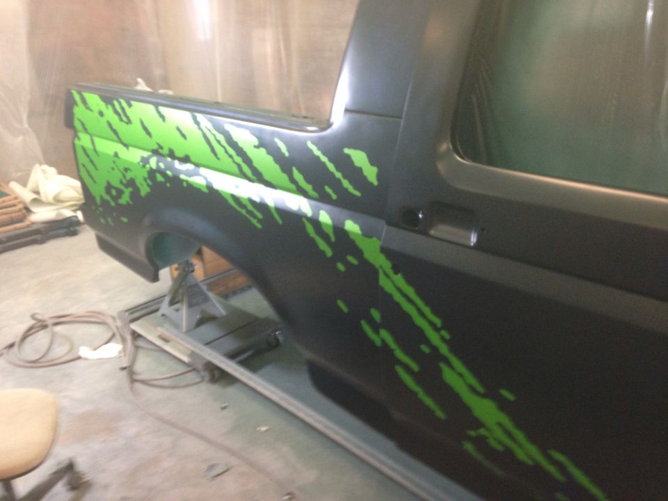 Black Ford Bronco with green splatter graphics, rear quarter panel visible, on jack stands
