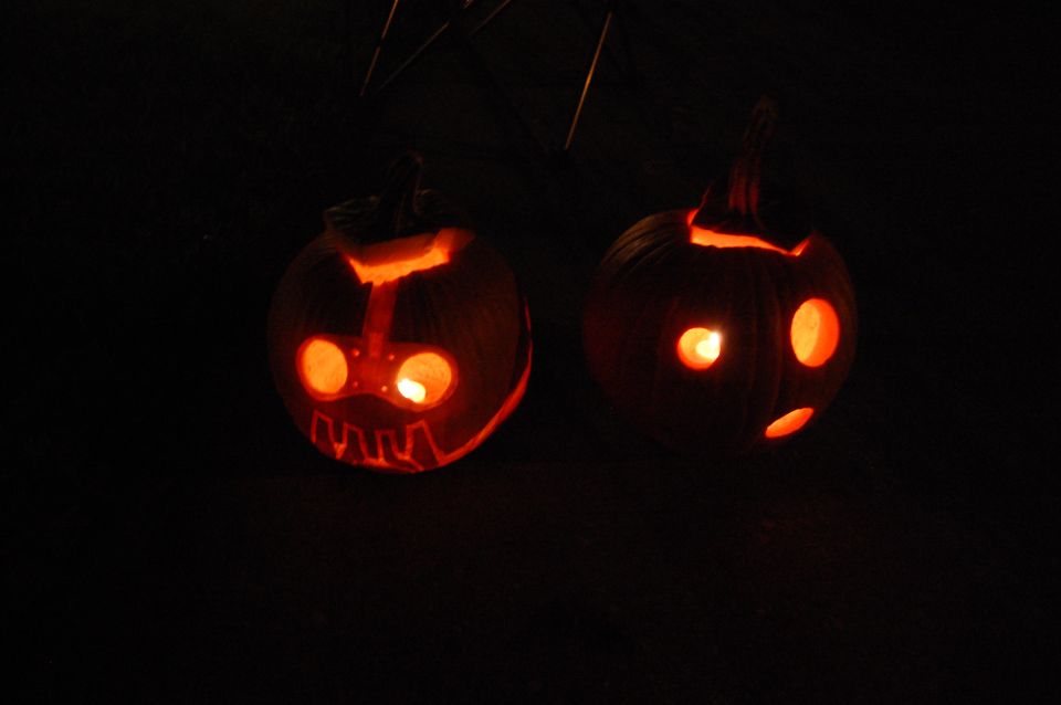 two carved pumpkins with glowing faces against a dark background