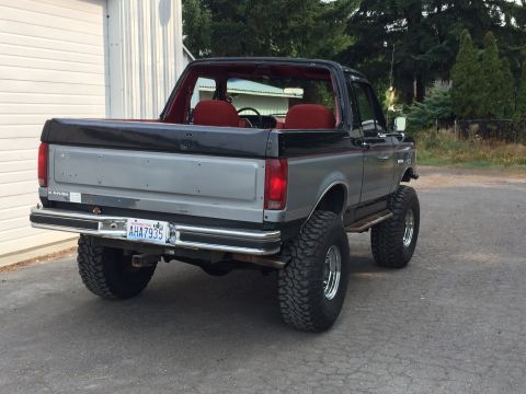 1989 Ford Bronco - Rear view of a lifted 1989 Ford Bronco with two-tone paint and red interior.