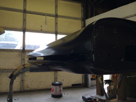 1989 Ford Bronco - A black car body panel is mounted on a stand in a workshop, with a large garage door visible behind it.