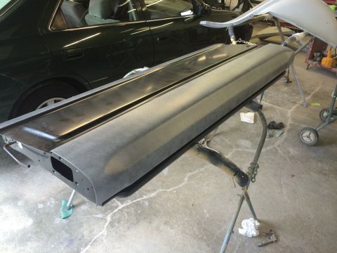 1989 Ford Bronco - Primed car tailgate resting on a stand in a workshop, with another vehicle visible behind it.