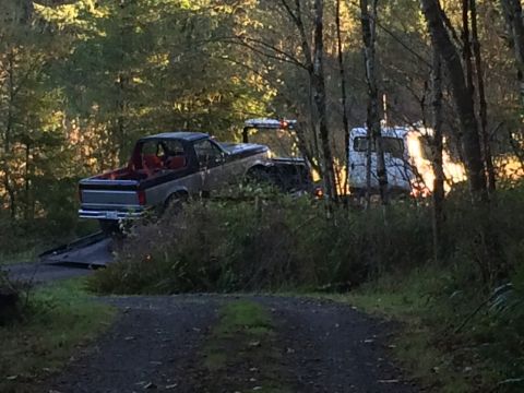 1989 Ford Bronco - Pickup truck being towed by an RV in a forest setting.