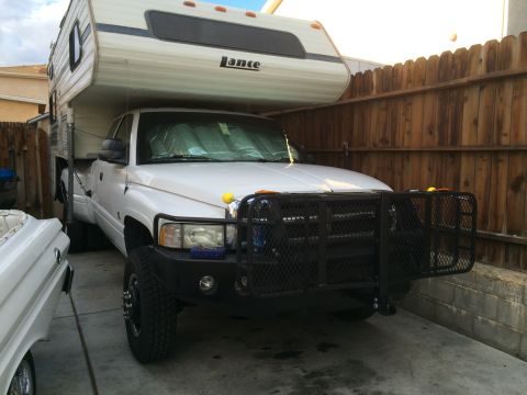 1997 Dodge 3500 - White pickup truck with a camper shell and a heavy-duty brush guard on the front bumper.