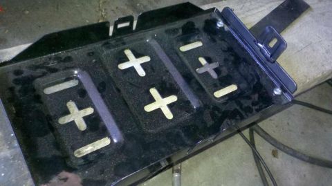 1982 Ford Bronco - A black metal battery tray with cutouts for positive and negative terminals is shown, possibly for a 1982 Ford Bronco. The tray is dusty an…