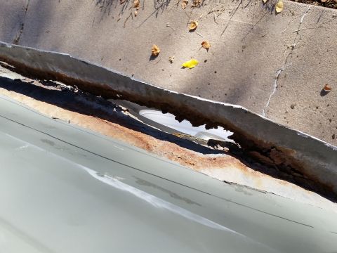 1988 Ford Bronco - A close-up shot of a heavily rusted and damaged metal gutter or flashing, possibly from a vehicle or building, resting on a concrete surfac…