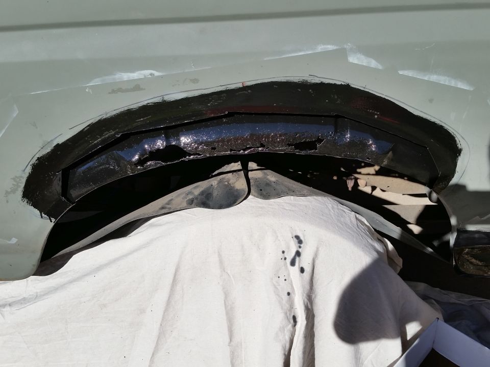 Close-up of a vehicle's wheel well opening with rust and black paint.