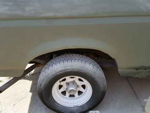 1988 Ford Bronco - The rear passenger side wheel and fender well of a light green vehicle are shown. The vehicle appears to be undergoing bodywork, with prime…