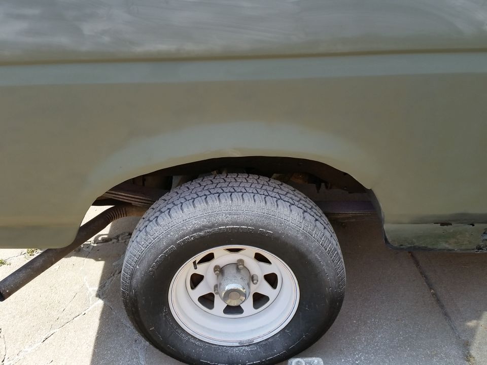 Rear passenger side wheel and fender well of a light green vehicle with primer visible.
