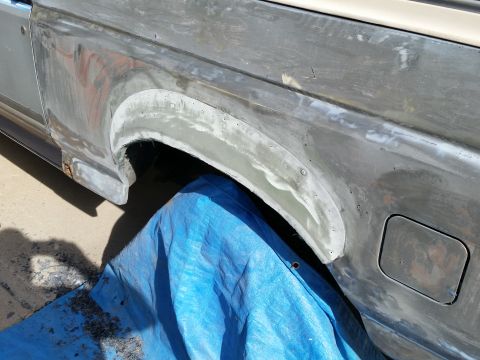 1988 Ford Bronco - A close-up view of the rear fender area of a vehicle undergoing bodywork. The metal is sanded and appears to have primer or filler applied,…