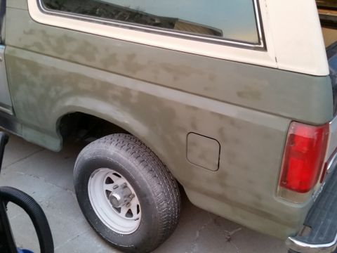 1988 Ford Bronco - Sanded rear quarter panel of a two-tone tan and green SUV with white steel wheel and red taillight.