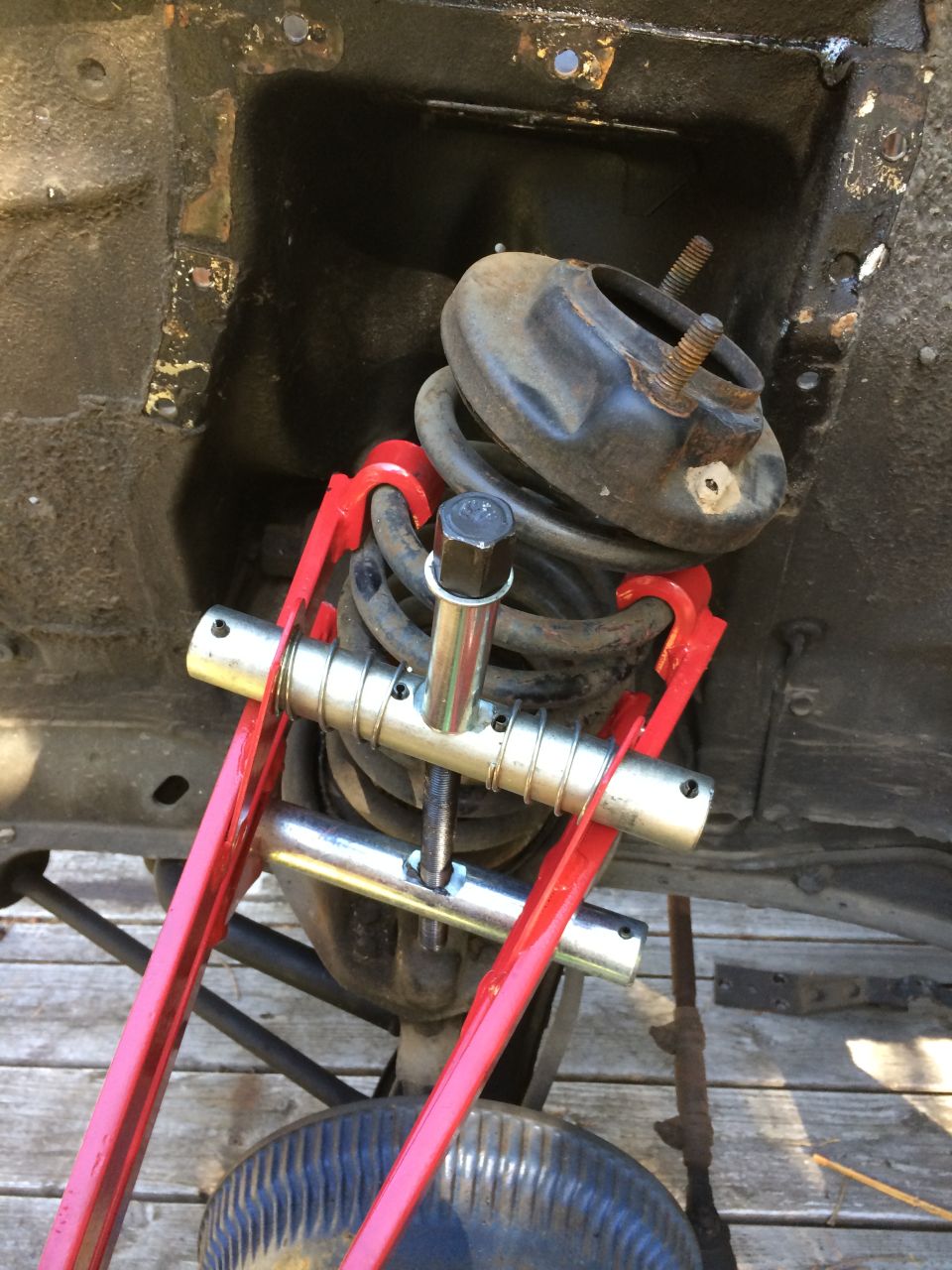 Red spring compressor tool on a vehicle's rear coil spring suspension.