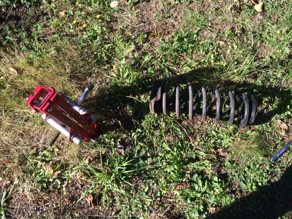 Red spring compressor tool and a detached coil spring on grass.