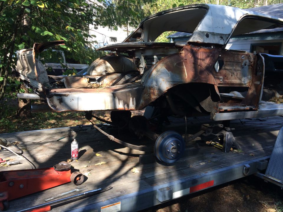 Heavily rusted vintage car body on a flatbed trailer with tools.