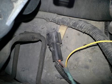 1991 Ford F-250 - A black electrical connector with a yellow wire attached is visible in an engine bay. The connector is plugged into a wiring harness covere…