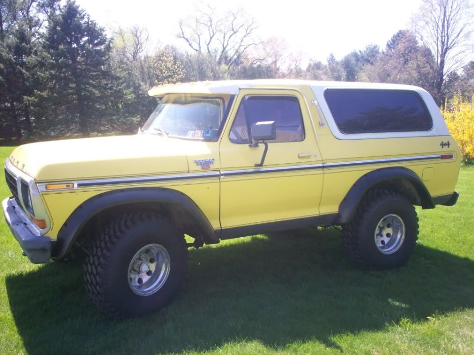 Yellow 1979 Ford Bronco with white top parked on grass