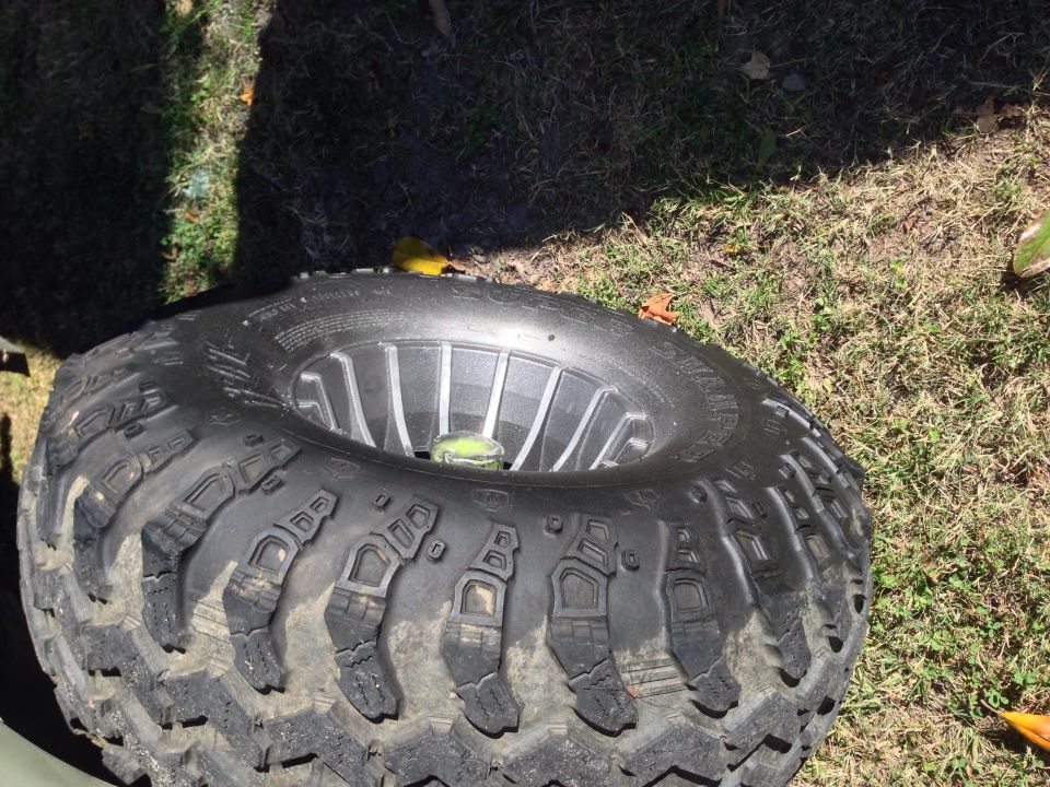 Off-road tire with aggressive tread pattern mounted on a silver wheel. Tire is resting on grass