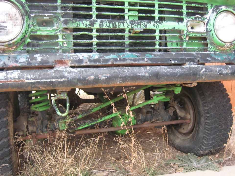 Green vintage Ford Bronco front end with tow hook and suspension details.
