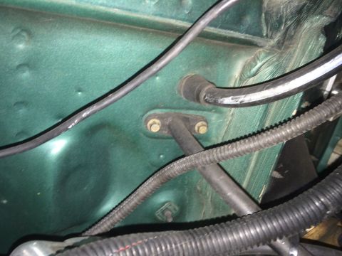 1990 Ford Bronco - A close-up view of the green painted firewall of a vehicle, showing various wires and hoses routed through grommets and secured with bolts.…