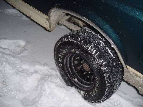 1993 Ford Bronco - A 1993 Ford Bronco's wheel and fender are visible, covered in snow.
