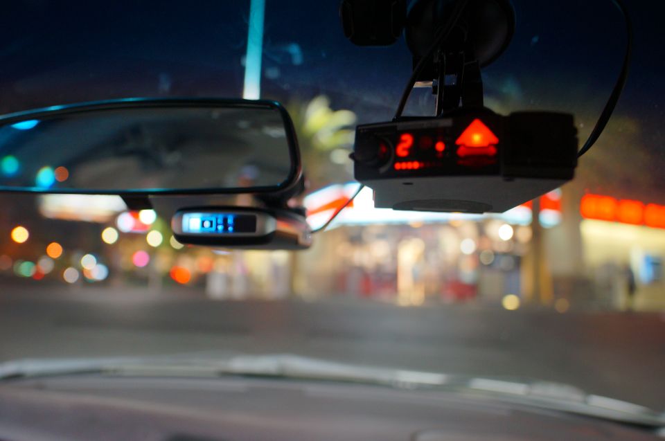 Radar detector with red lights and a blue display next to a rearview mirror