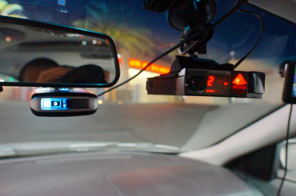 Radar detector with red digital display and GPS device with blue display mounted on windshield