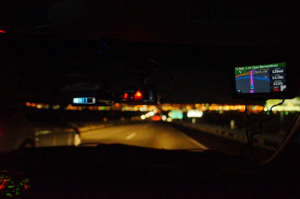 Car interior at night, dashboard with GPS and radar detector visible, highway lights in distance