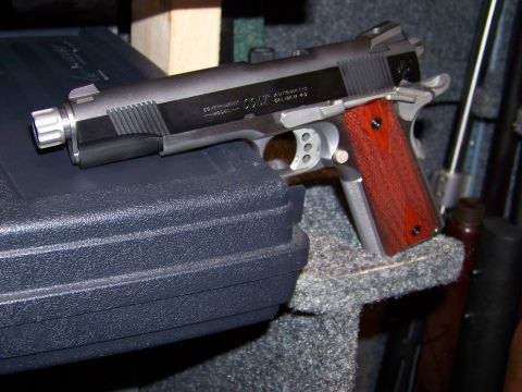 1995 Mercury Grand Marquis - A Colt Government Automatic .45 pistol with distinctive wooden grips and a threaded barrel is displayed.