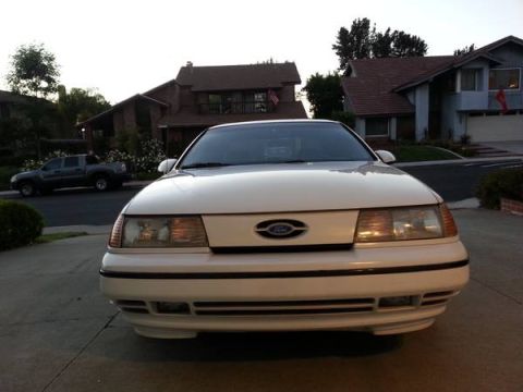 1993 Ford Taurus - Front view of a white 1993 Ford Taurus parked in a driveway with a pickup truck in the background.