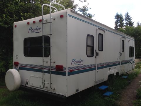 1988 Ford F-350 - This RV trailer is parked outdoors with trees in the background and grass around its base.